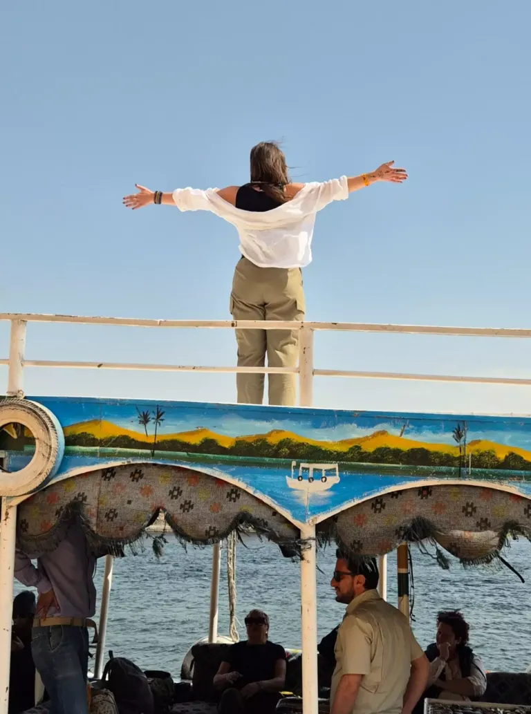 Mujer mirando al cielo con los brazos abiertos subida a un barco